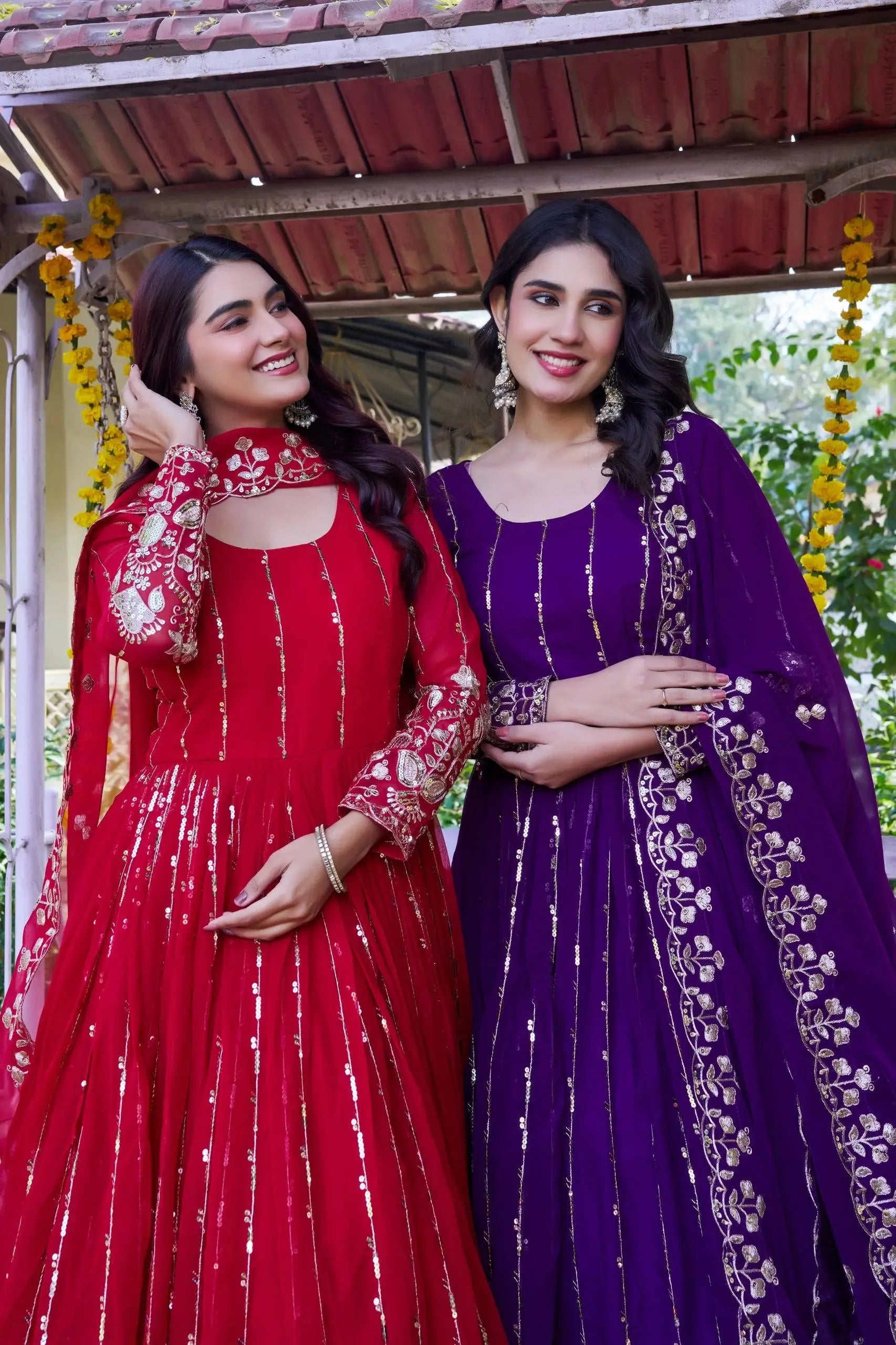 Two women in traditional red and purple dresses standing together outdoors.